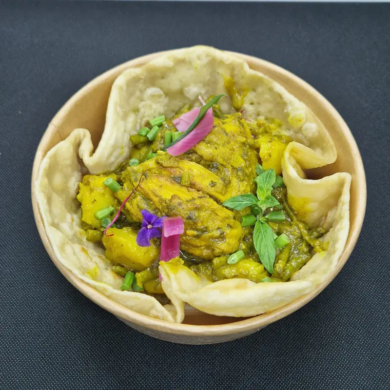 Un curry doré au poulet et aux pommes de terre, servi dans un bol de pain croustillant et décoré de fleurs comestibles.