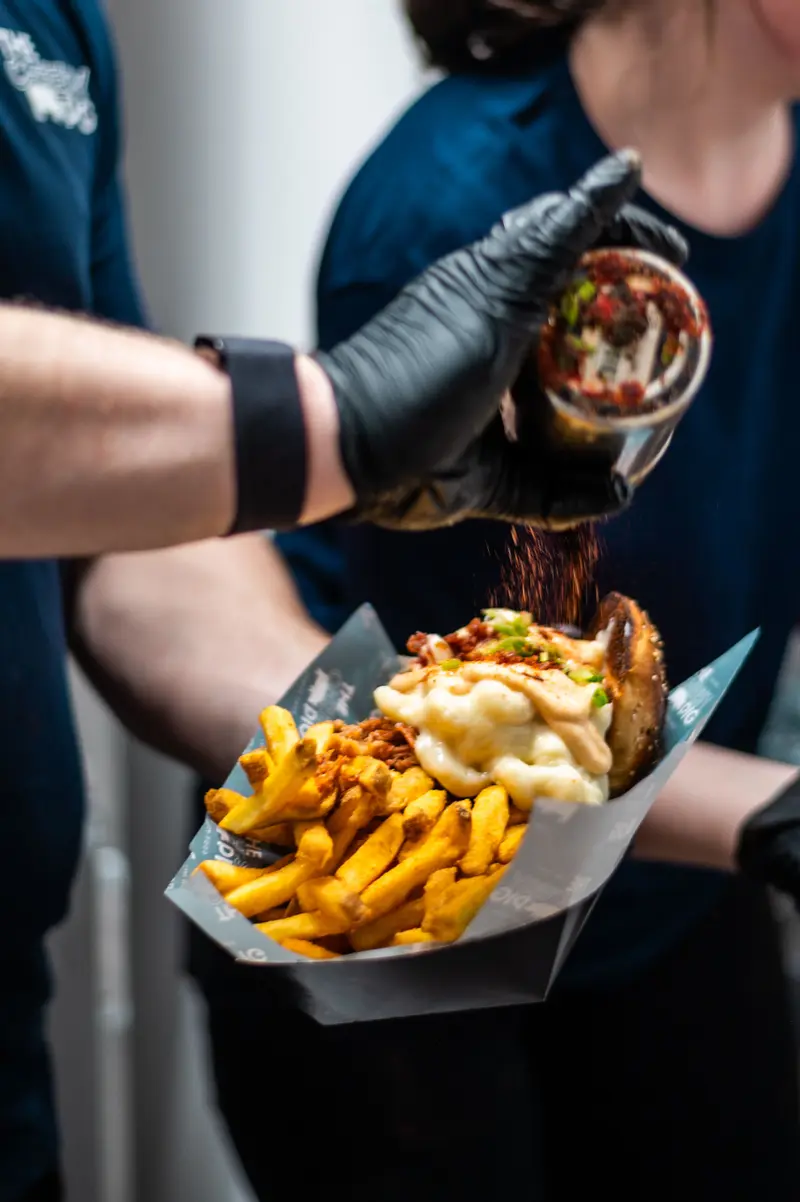 Des frites garnies de viande effilochée et de sauce fromagère, servies dans un cornet en papier pendant l'assaisonnement final par l'équipe du truck.
